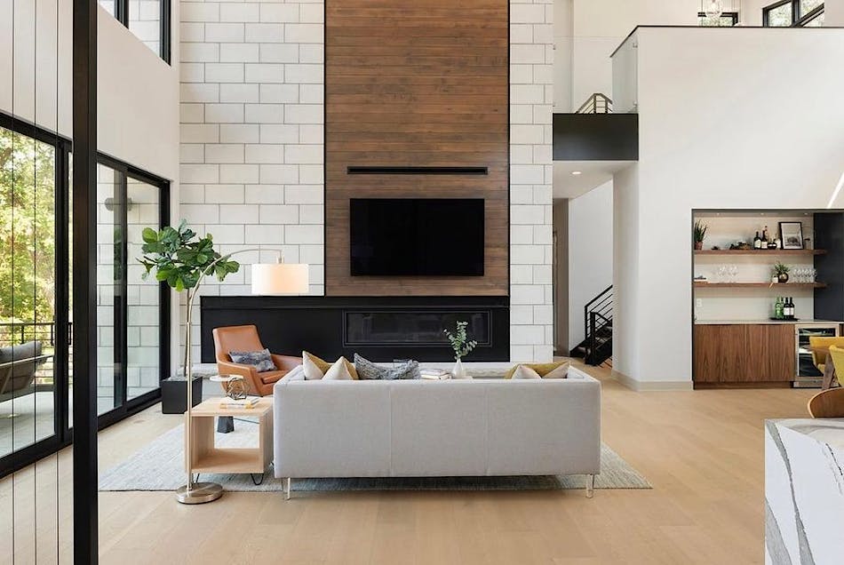 This living room space features a white masonry veneer wall with a wood fireplace. There is a gray sofa in the space, along with a gold lamp, a wood side table and a leather chair.