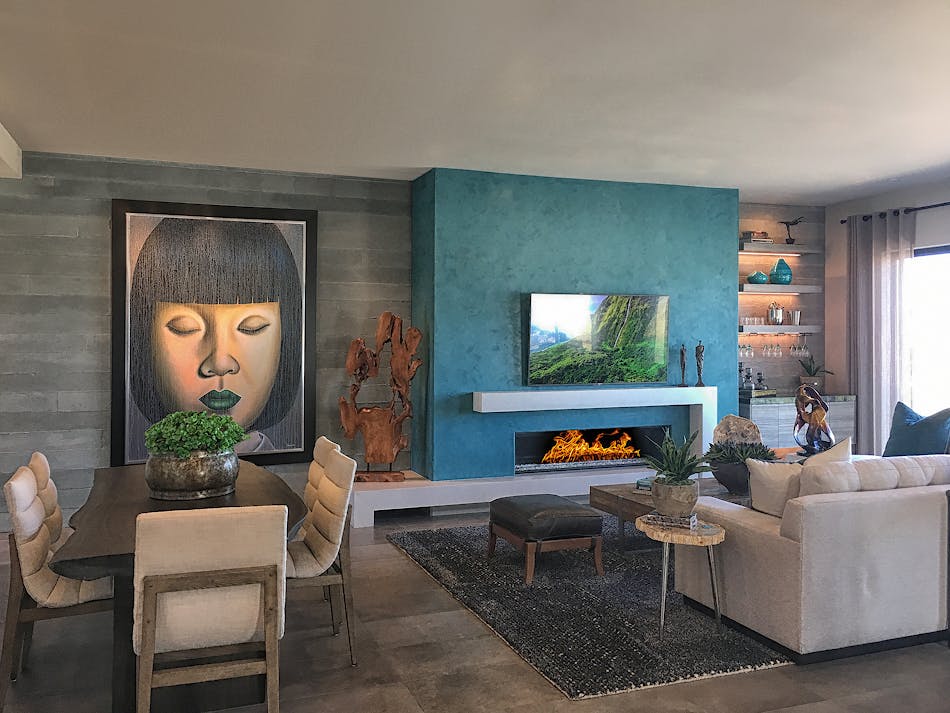 A modern living area with a couch, dining table and gas fireplace. There are multiple pieces of art and sculpture around the room and a blue accent wall behind the fireplace.