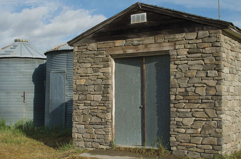 A stone shed with gray double doors next to two metal water tanks.