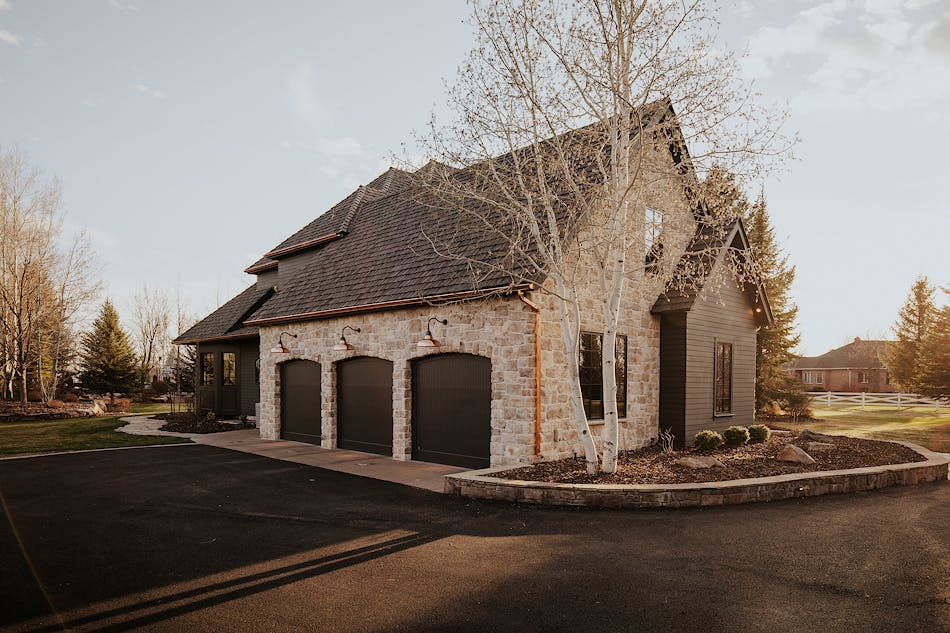 This house features a three-car garage with stone veneer siding. There is a green lawn in front of the home and a paved driveway that loops around to the back.