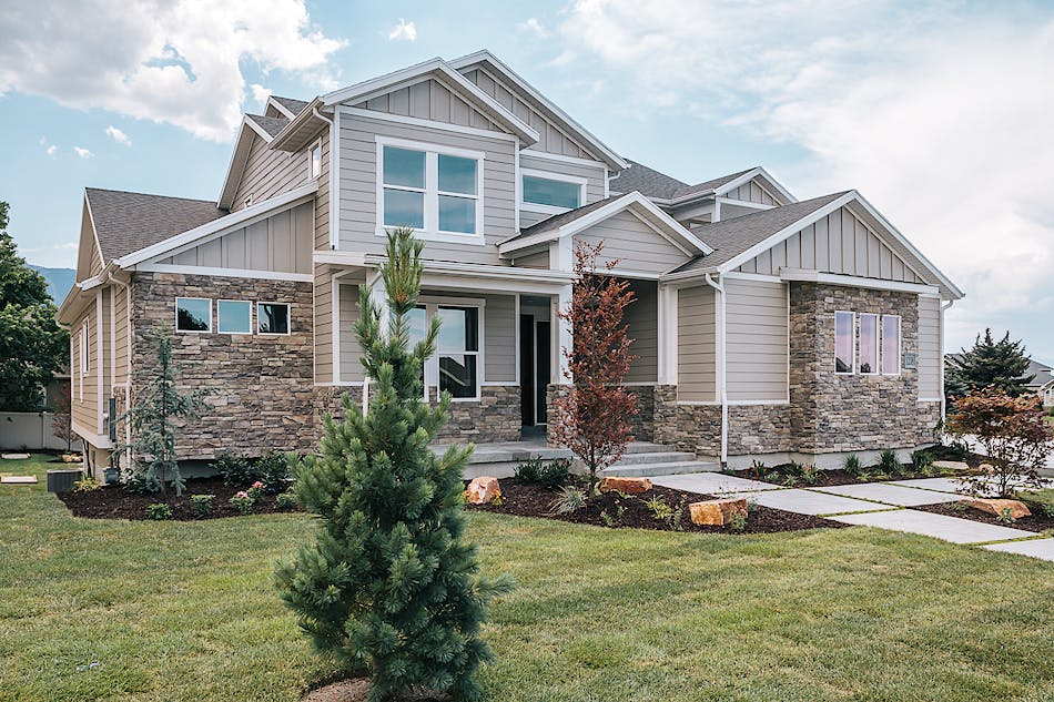 The view of the front of a home. The home has exposed stone and white trim with a large front yard and front walkway.