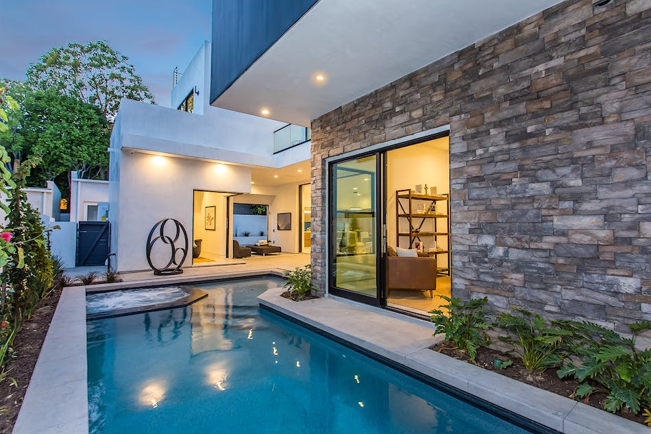 This outdoor area features a swimming pool and plants surrounding the pool’s perimeter. There is a sliding door that offers easy access from the indoor living room to the outdoor space.