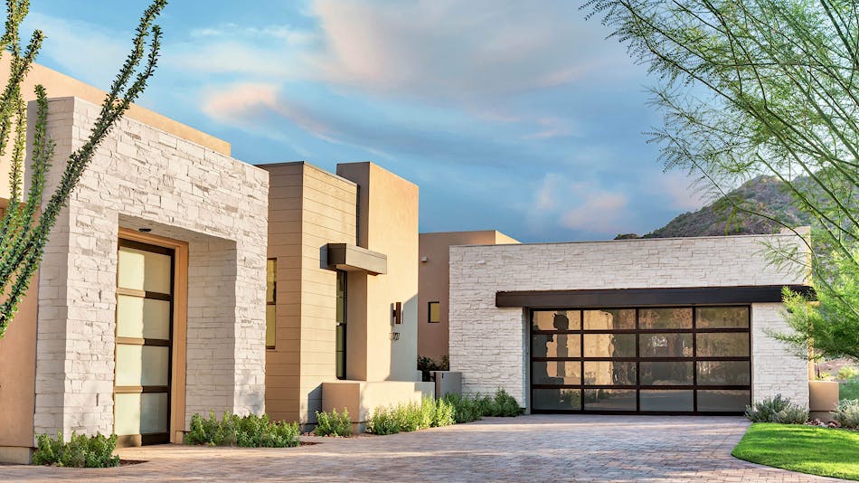 A modern home with exterior accents of white stone veneer. The home has a cobblestone driveway.