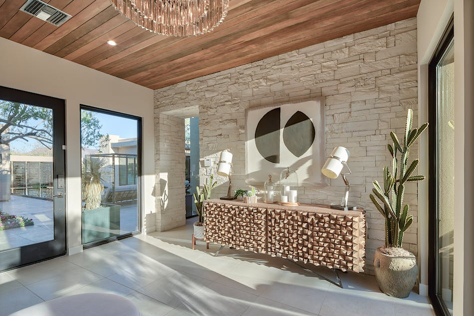 An foyer designed with white stone veneer. There is a buffet table, cactus plants, artwork and lamps in the space.