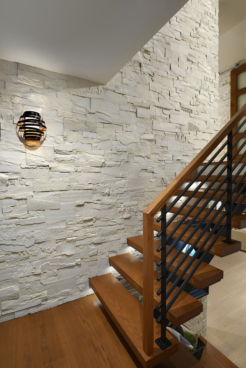 A staircase features white stone veneer on the wall. There are wooden steps leading to the upstairs of the home.