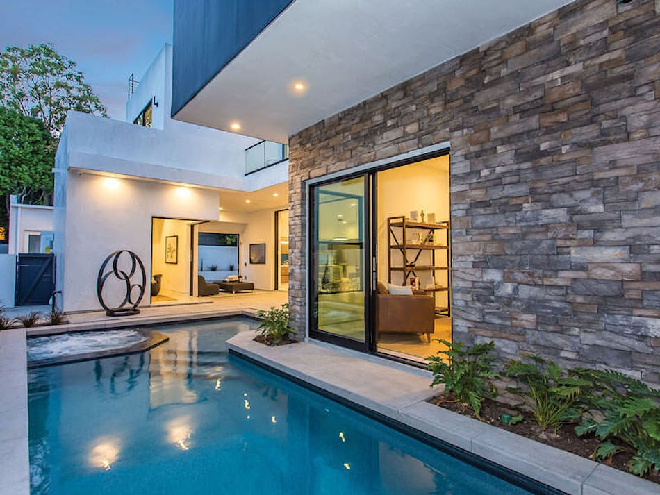 This house features masonry veneer from Creative Mines. There is a pool located in the backyard, and a sliding glass door leads inside to a living area.