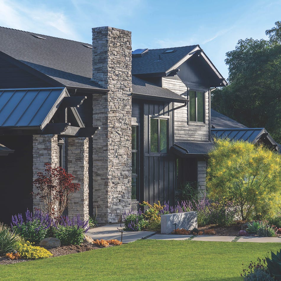 A modern farmhouse features black painted wood, a black metal roof and strong stone accents for the grand entrance and fireplace detail.