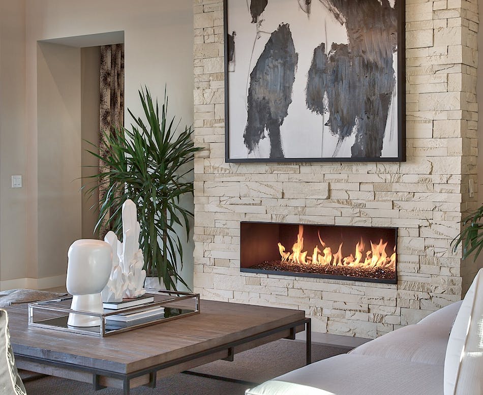 A beige stone veneer fireplace with abstract art framed above it and a coffee table with white abstract figurines.