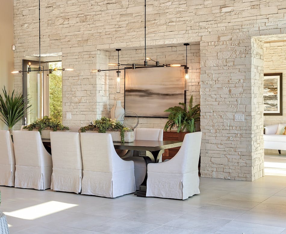 A dining room featuring a white interior stone veneer accent wall with a dining room table and six white chairs.
