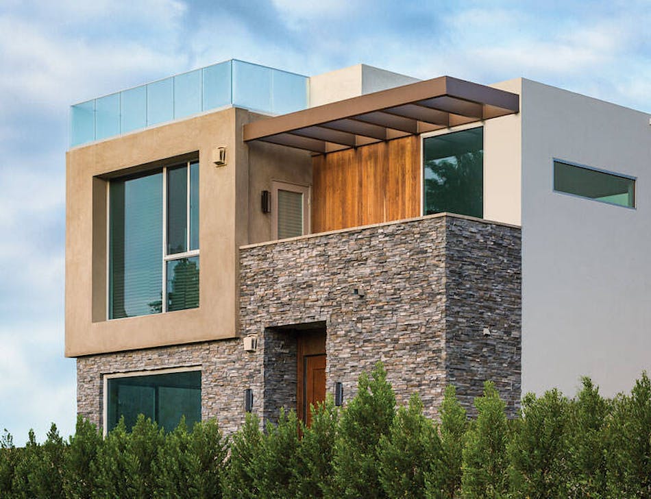 This modern rectangular home features concrete, wood and stone veneer accents on the siding. There are green trees surrounding the perimeter of the home.
