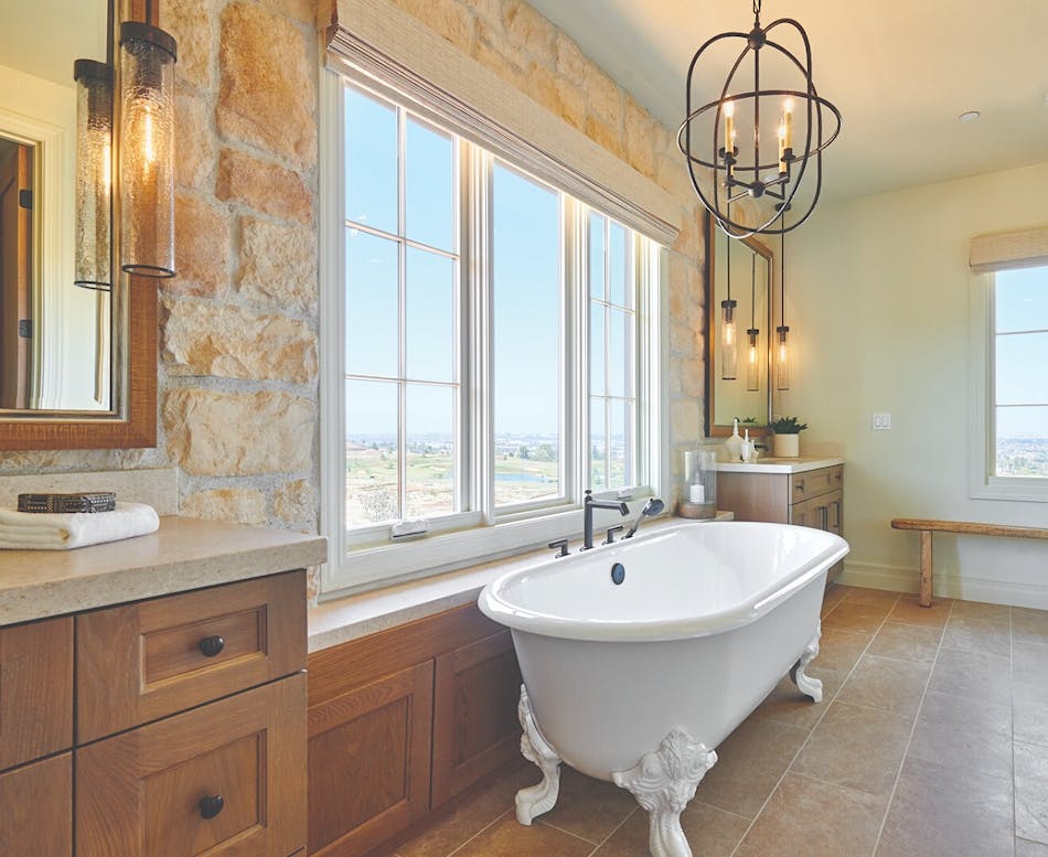 Stone veneer accent wall in bathroom with white clawfoot bathtub and extra large window that looks out over the plains.