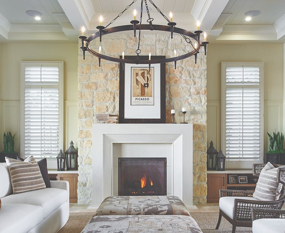 This living room features a stone veneer fireplace, a white sofa, two gray chairs and a hanging chandelier.