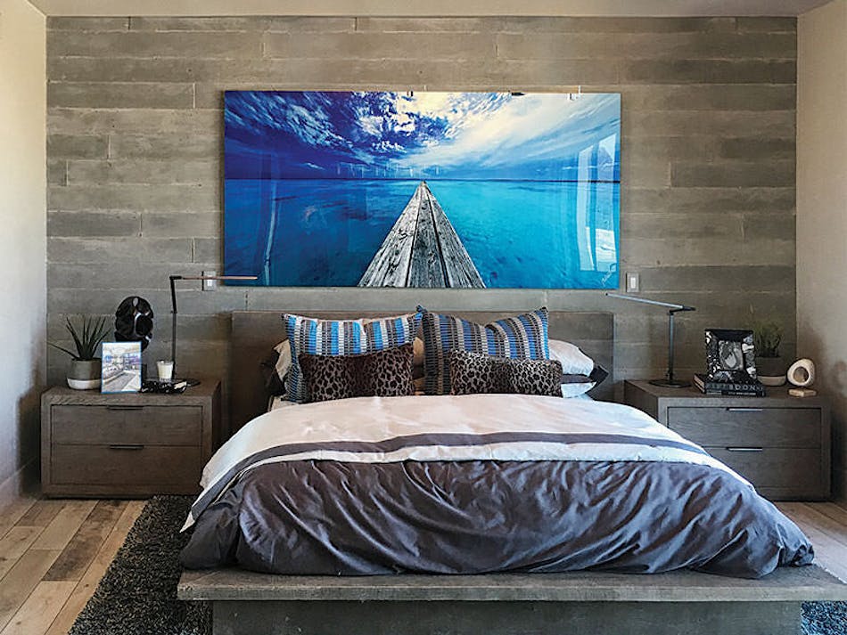 A gray bedroom with a wood veneer accent wall behind the headboard of the bed. There is a bright blue colored landscape picture above the headboard.