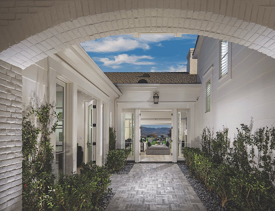 This entryway features a white brick veneer. There are green plants to the right and left of the walkway leading to the front door.