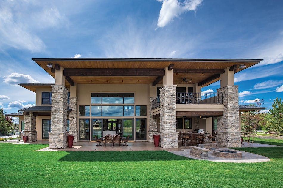 The view of the back of a modern home. The home incorporates multiple stone veneer columns and large windows.
