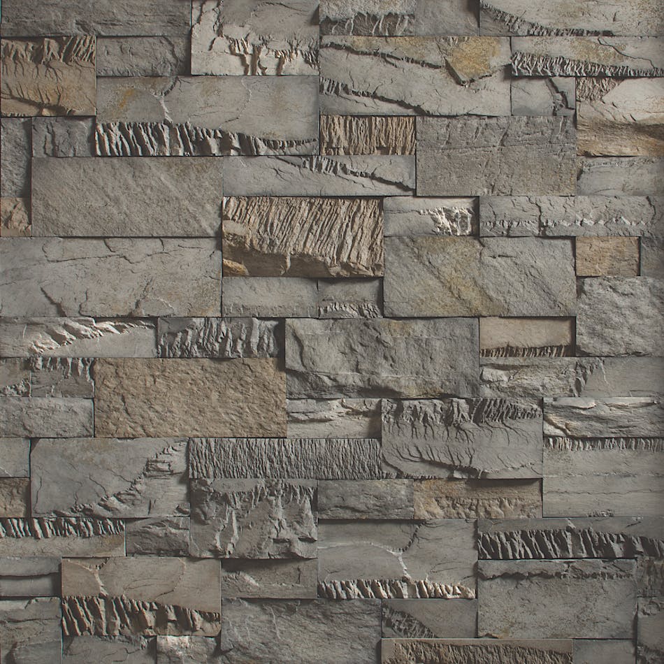An image of a dark gray and tan stone wall. The wall is made of chopped stone and the pieces of stone are a variety of sizes.